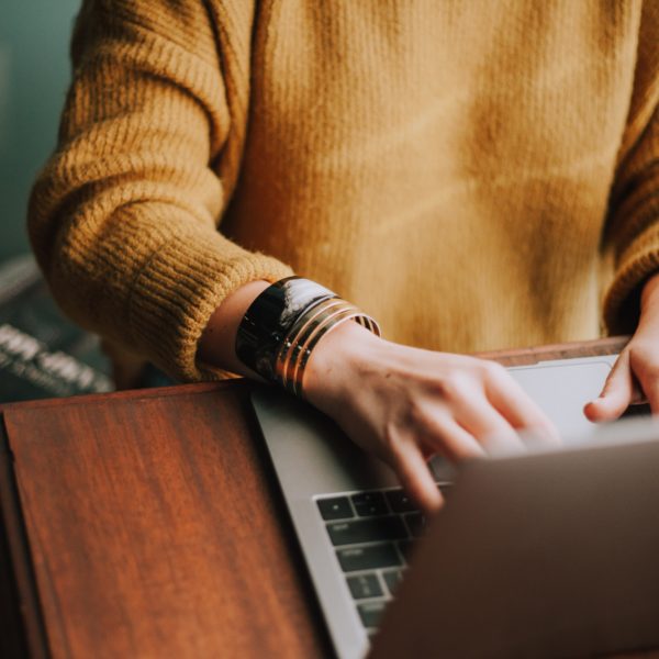 girl in a yellow sweater typing at a laptop